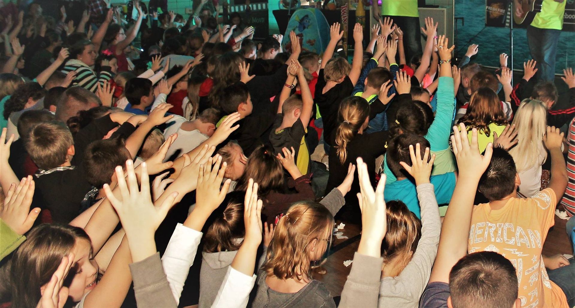 Crowd with arms raised in a brightly lit room.