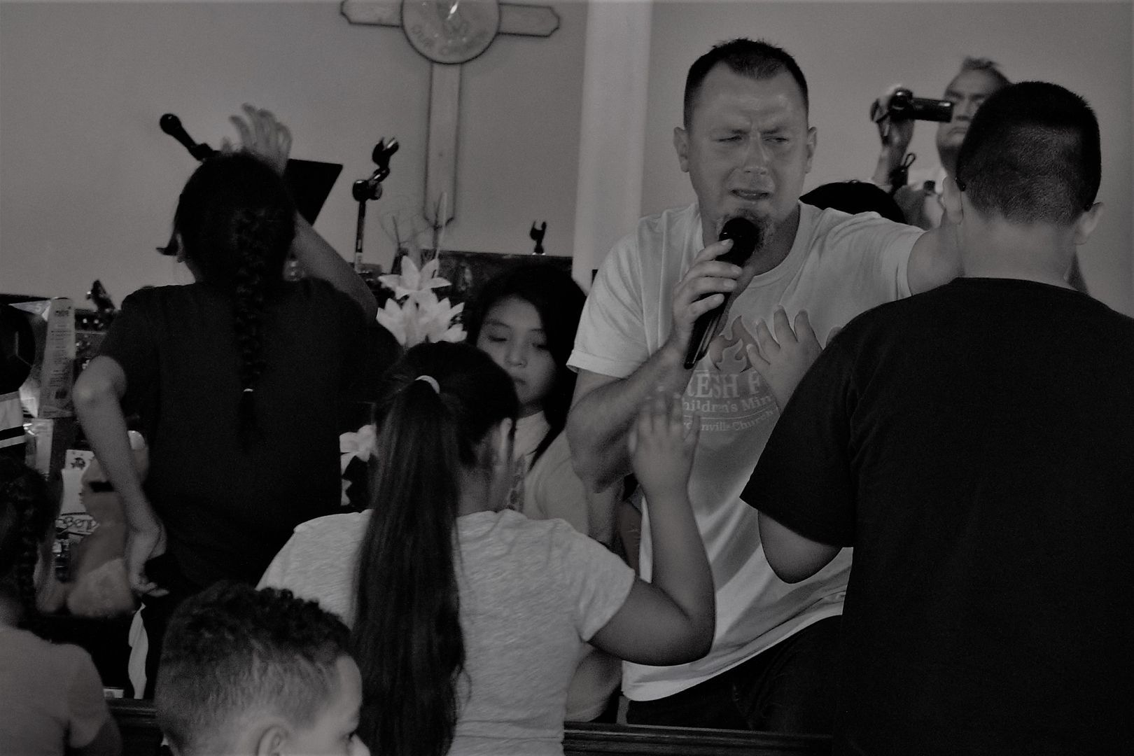 Man with microphone speaking to a crowd, possibly a church service. Black and white.