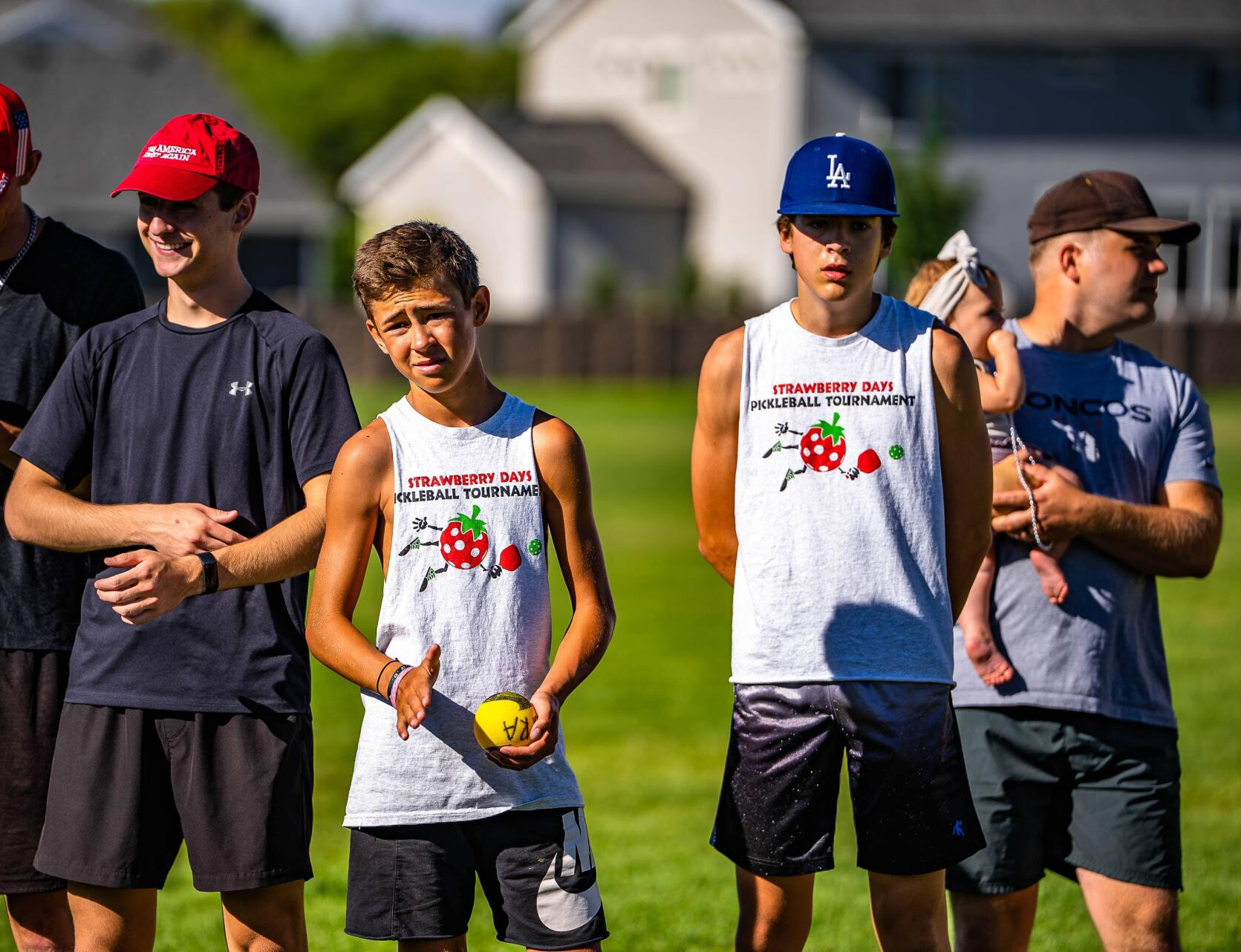 Group of people outdoors wearing athletic clothing; two in matching white tank tops with strawberry logo.