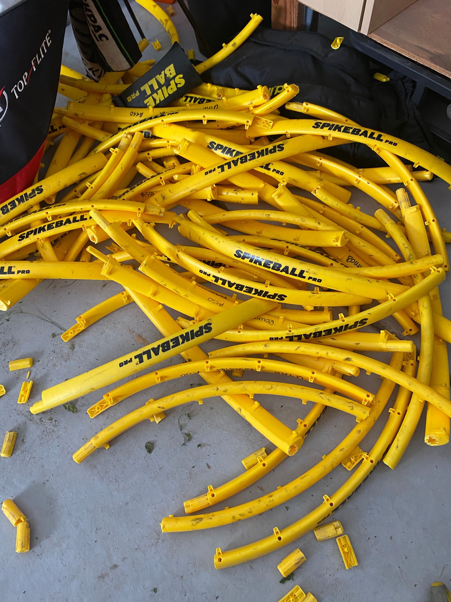 Pile of yellow Spikeball frame pieces on a concrete surface, some broken.