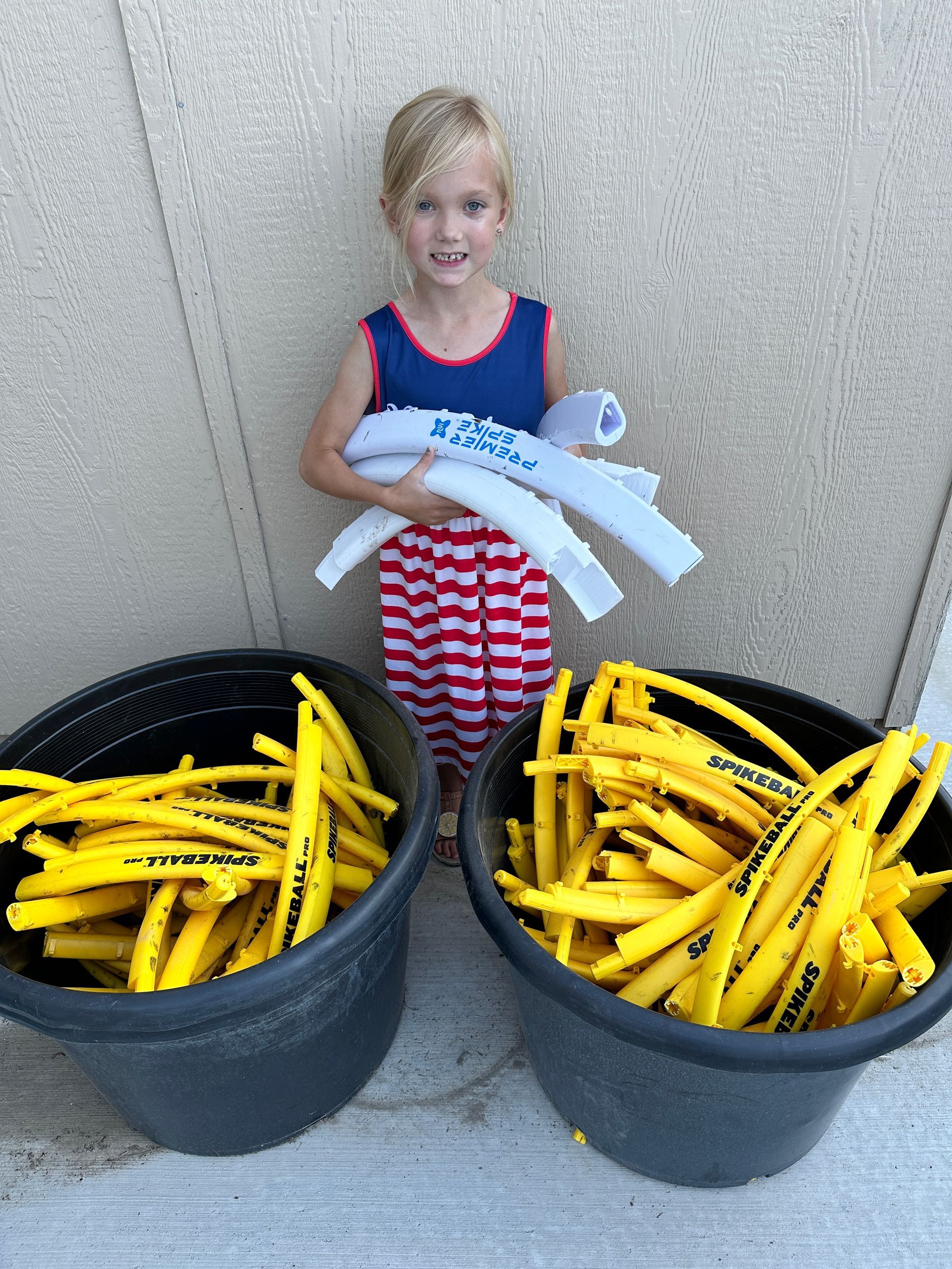 Young girl holding white pool noodles stands between two tubs of yellow noodles.