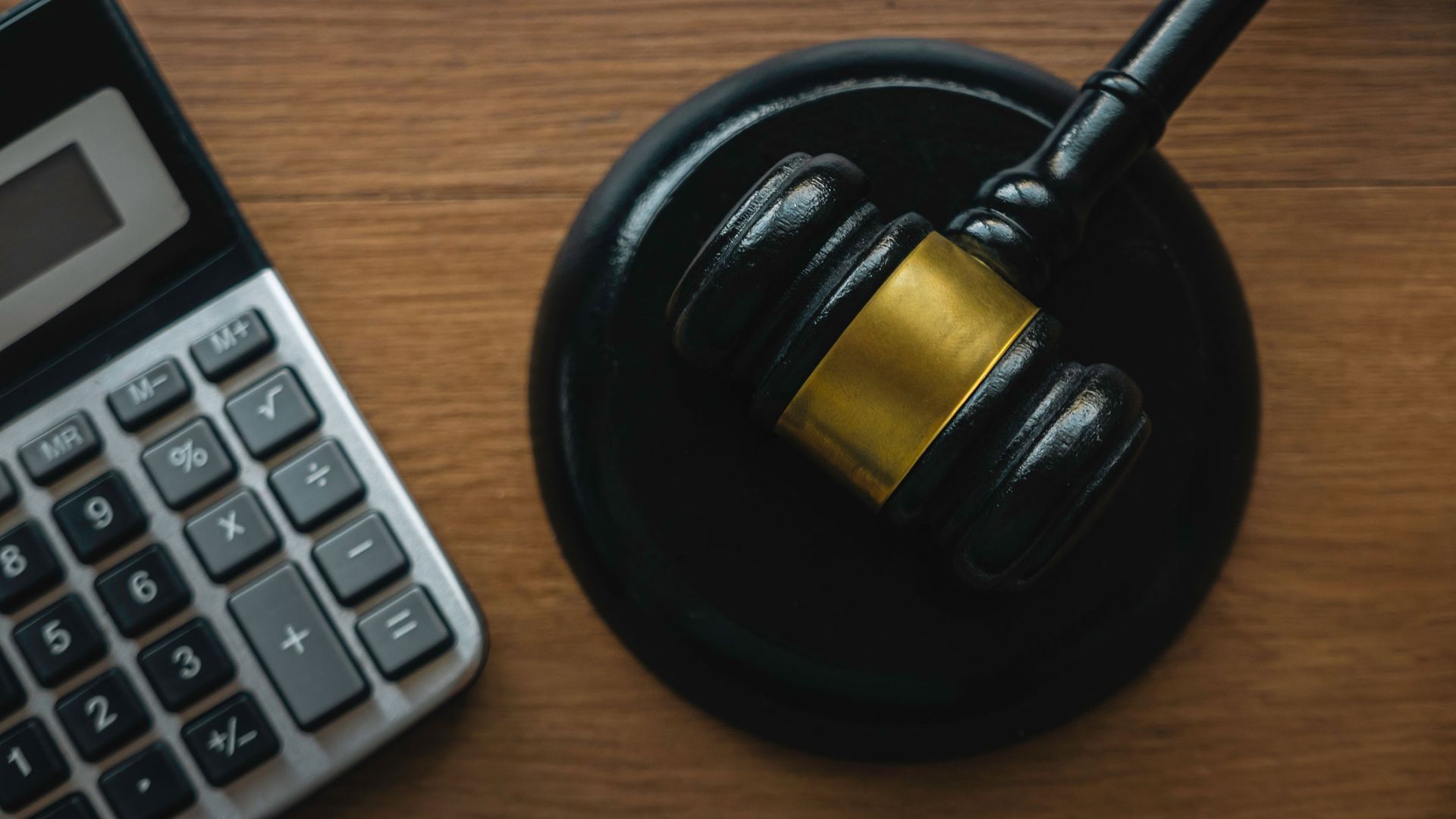 Calculator and judge's gavel on a wooden surface.