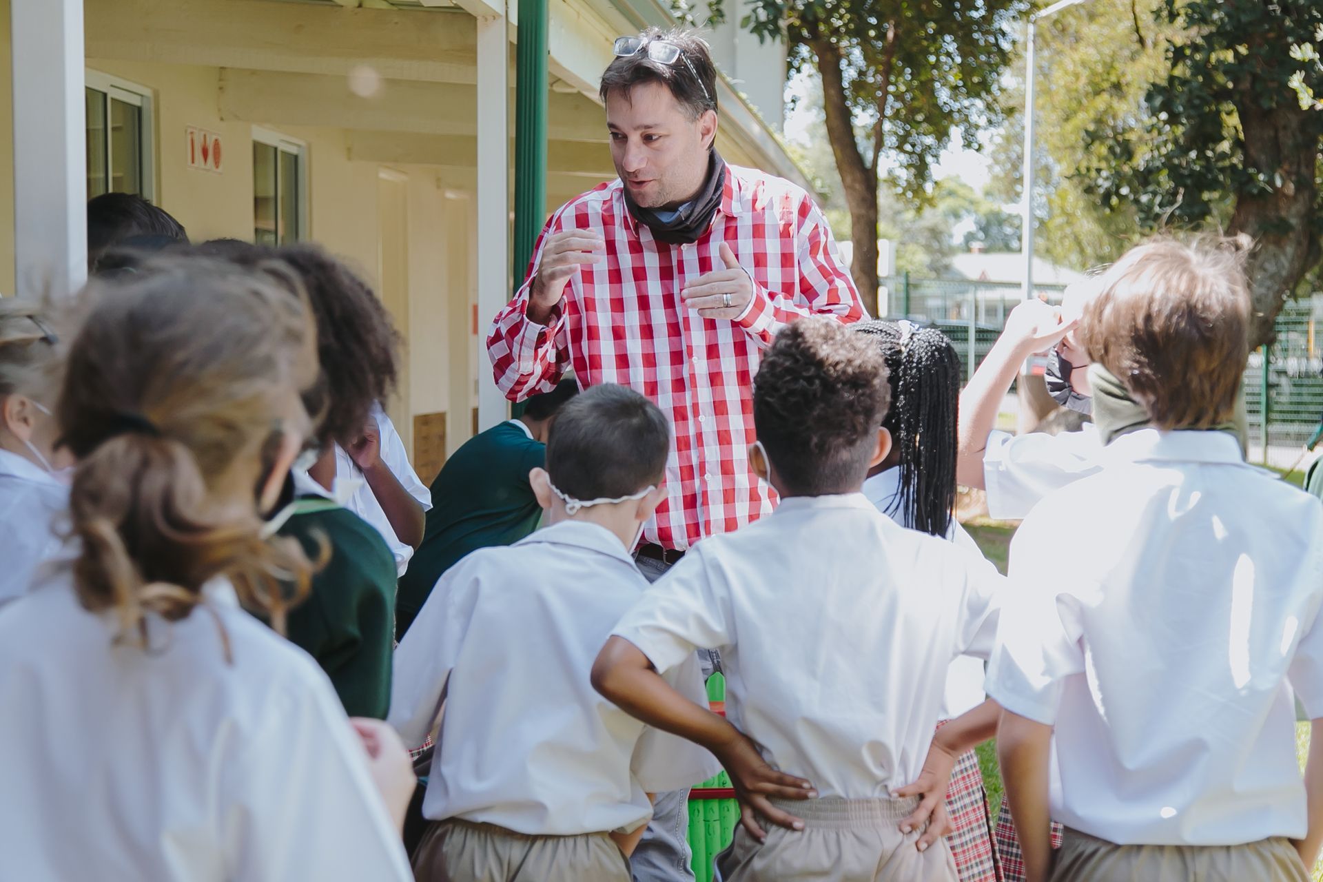 A man in a plaid shirt is talking to a group of children.