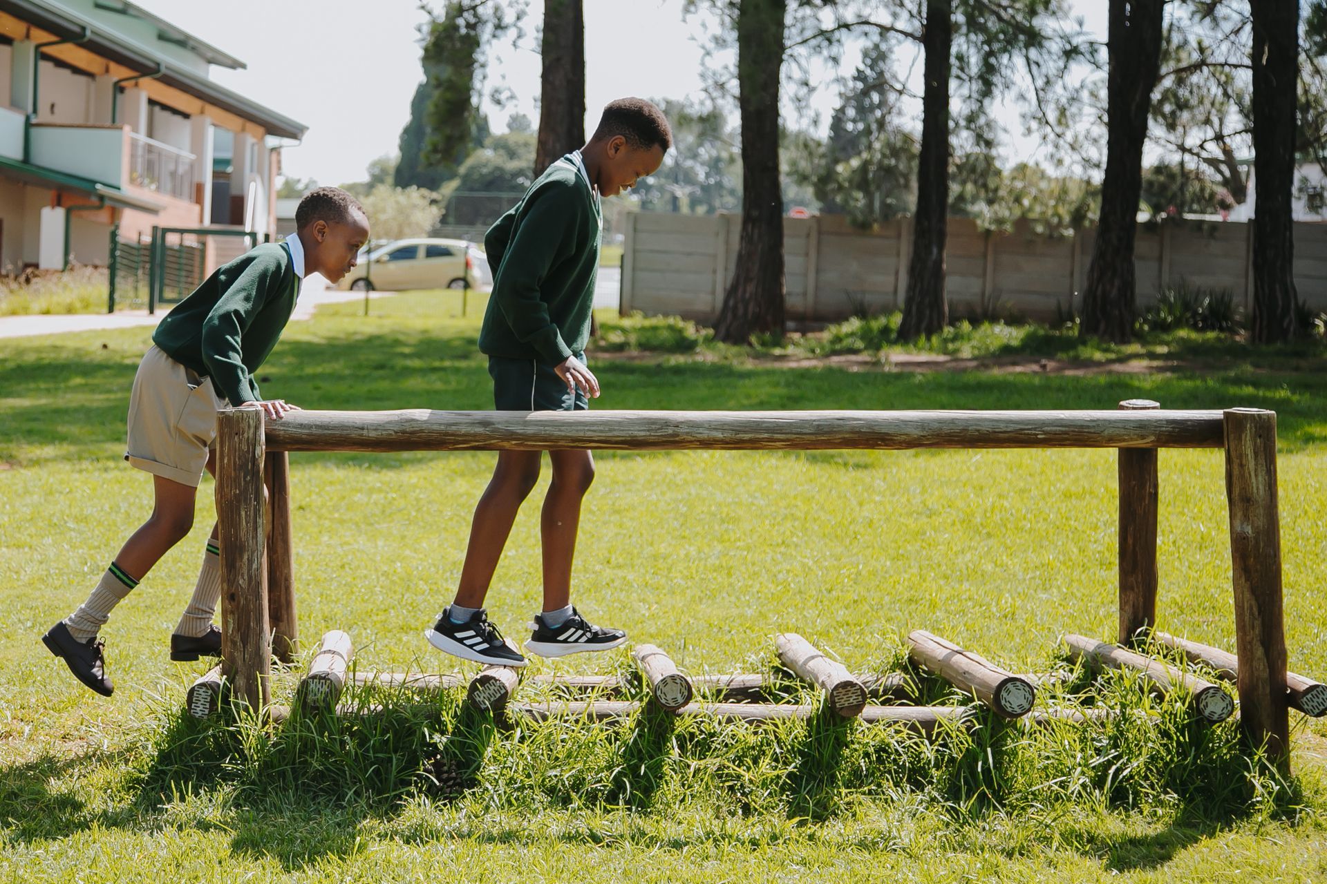 Two young boys are playing on a wooden obstacle course in a park.