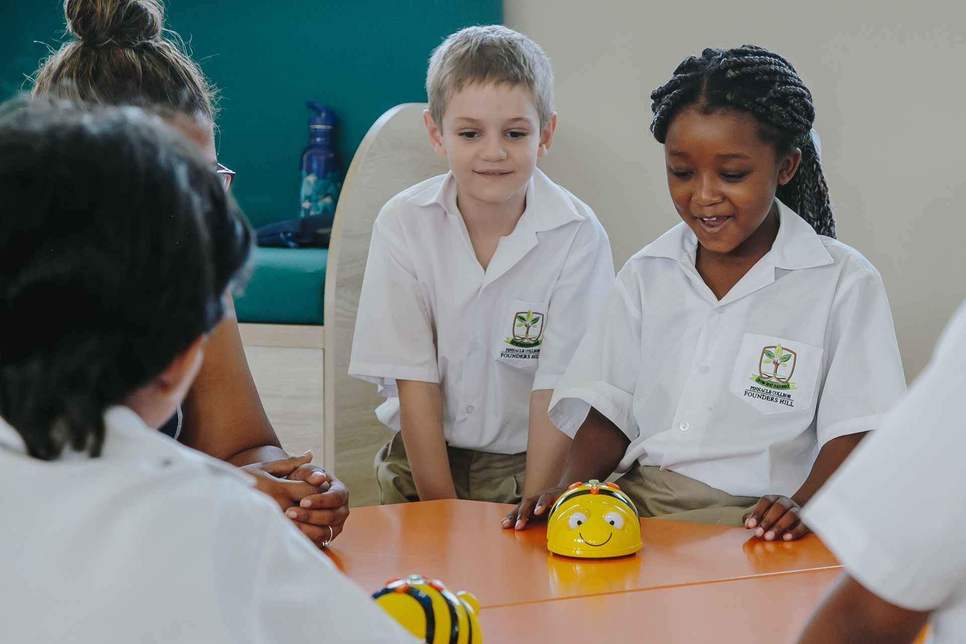 A group of children are sitting around a table playing with a robot.