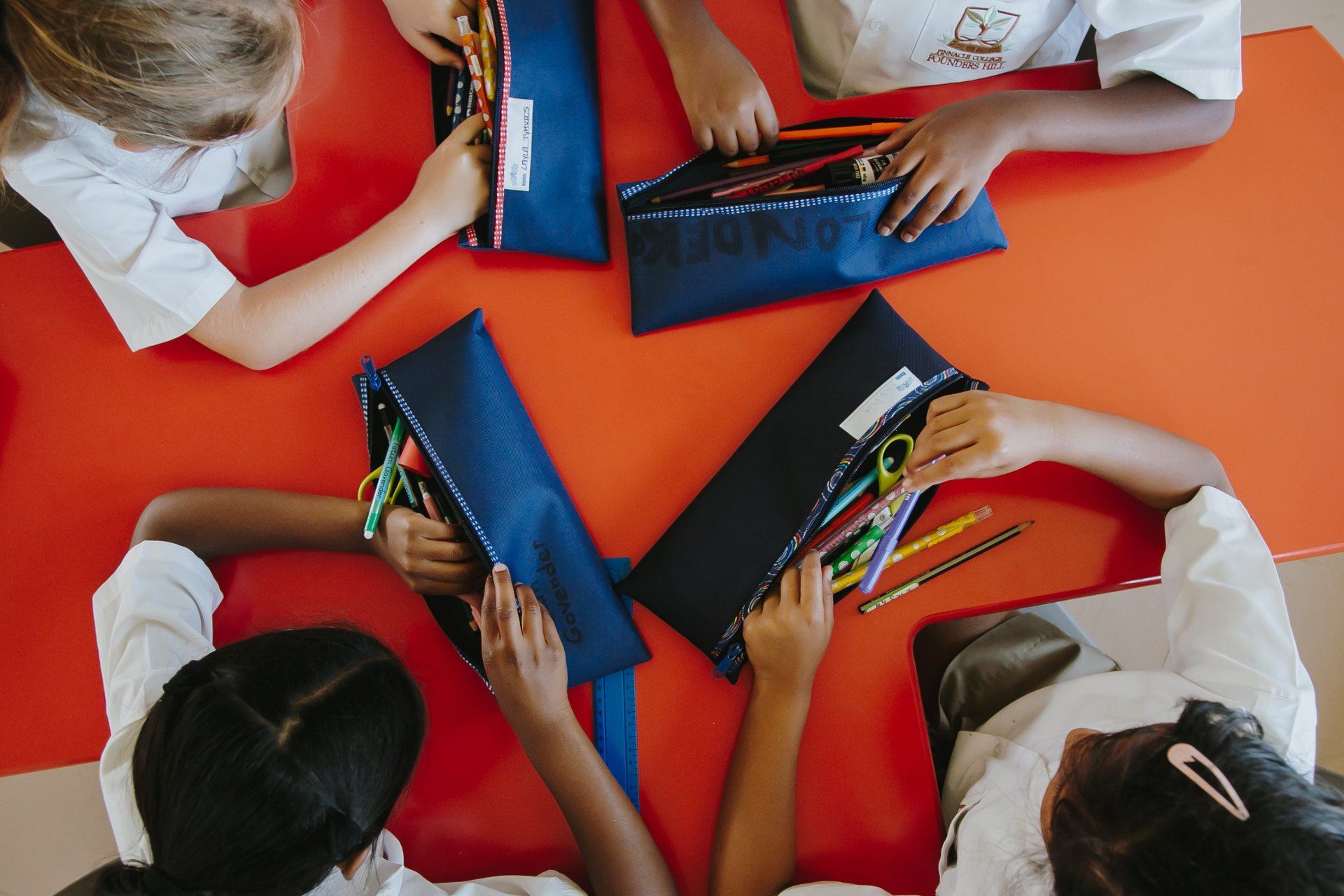 A group of children are sitting around a table holding pencil cases.