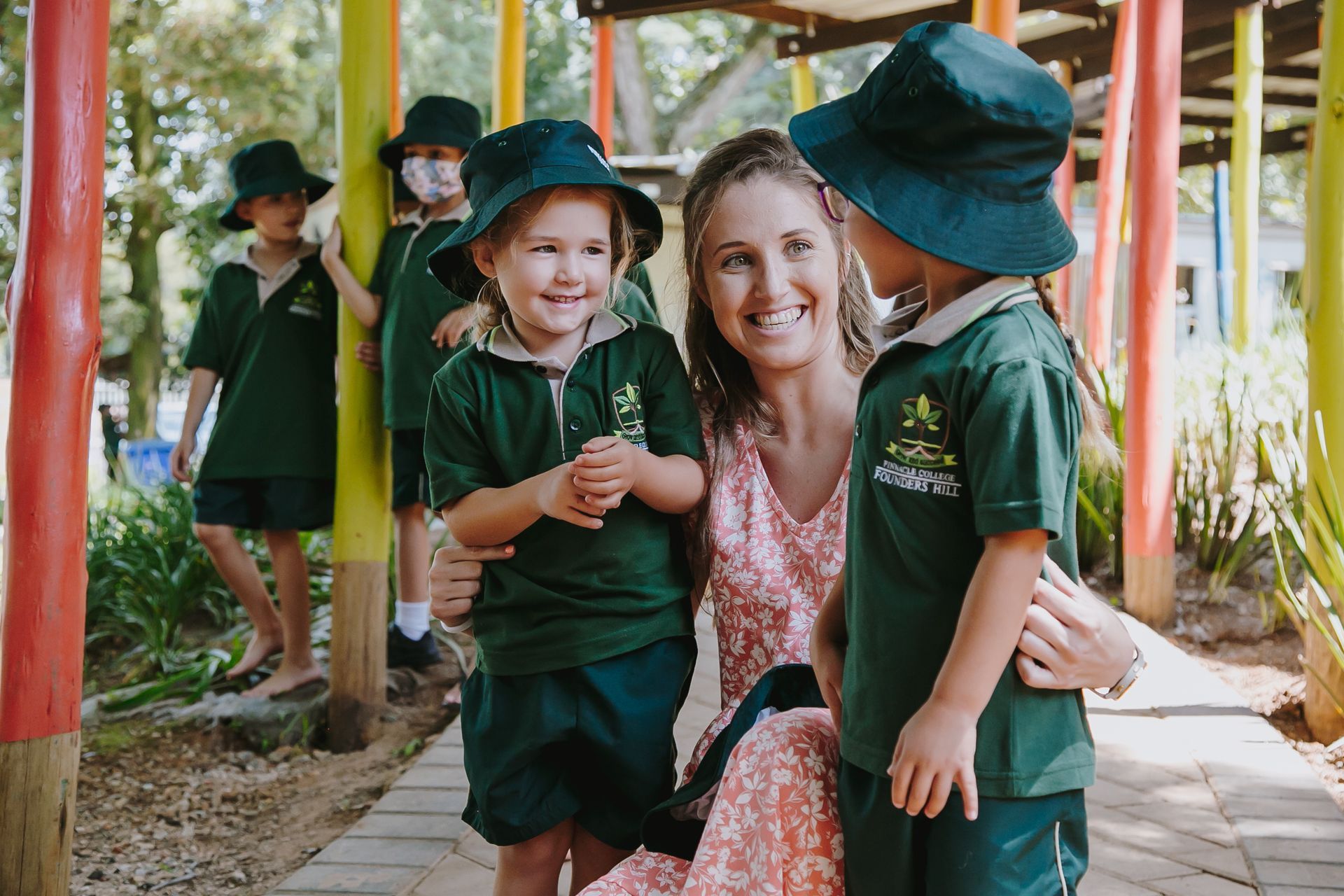 A woman is kneeling down next to two children in school uniforms.