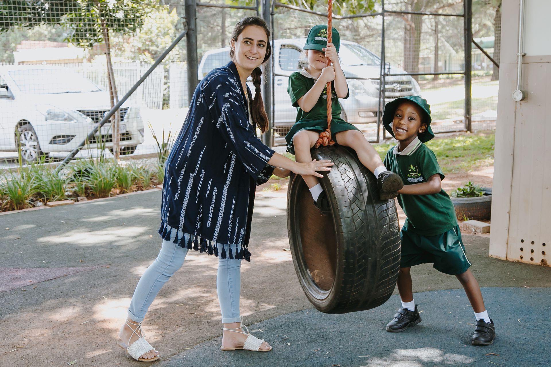 A woman and two children are playing on a tire swing.