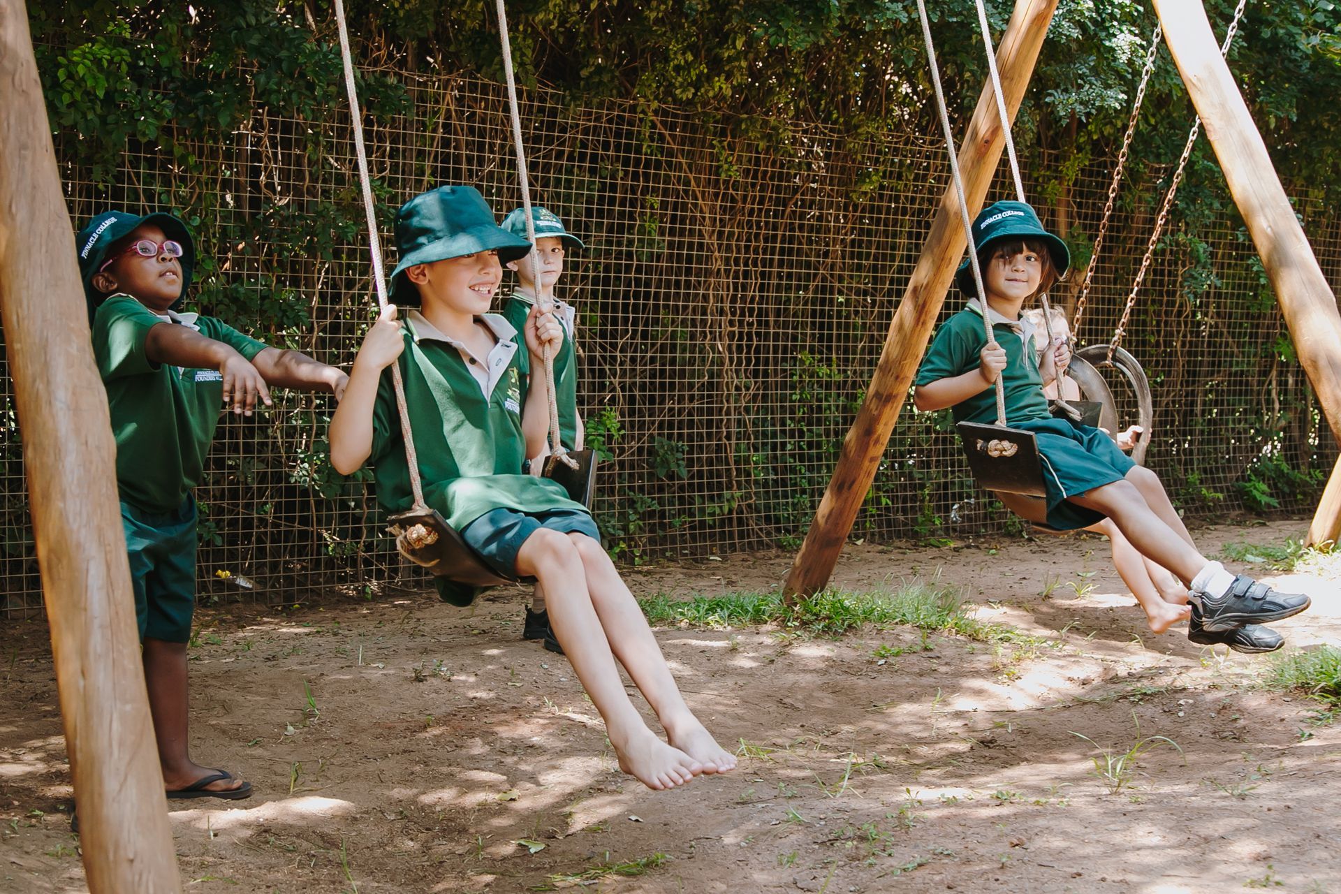 Three children are sitting on swings in a playground.