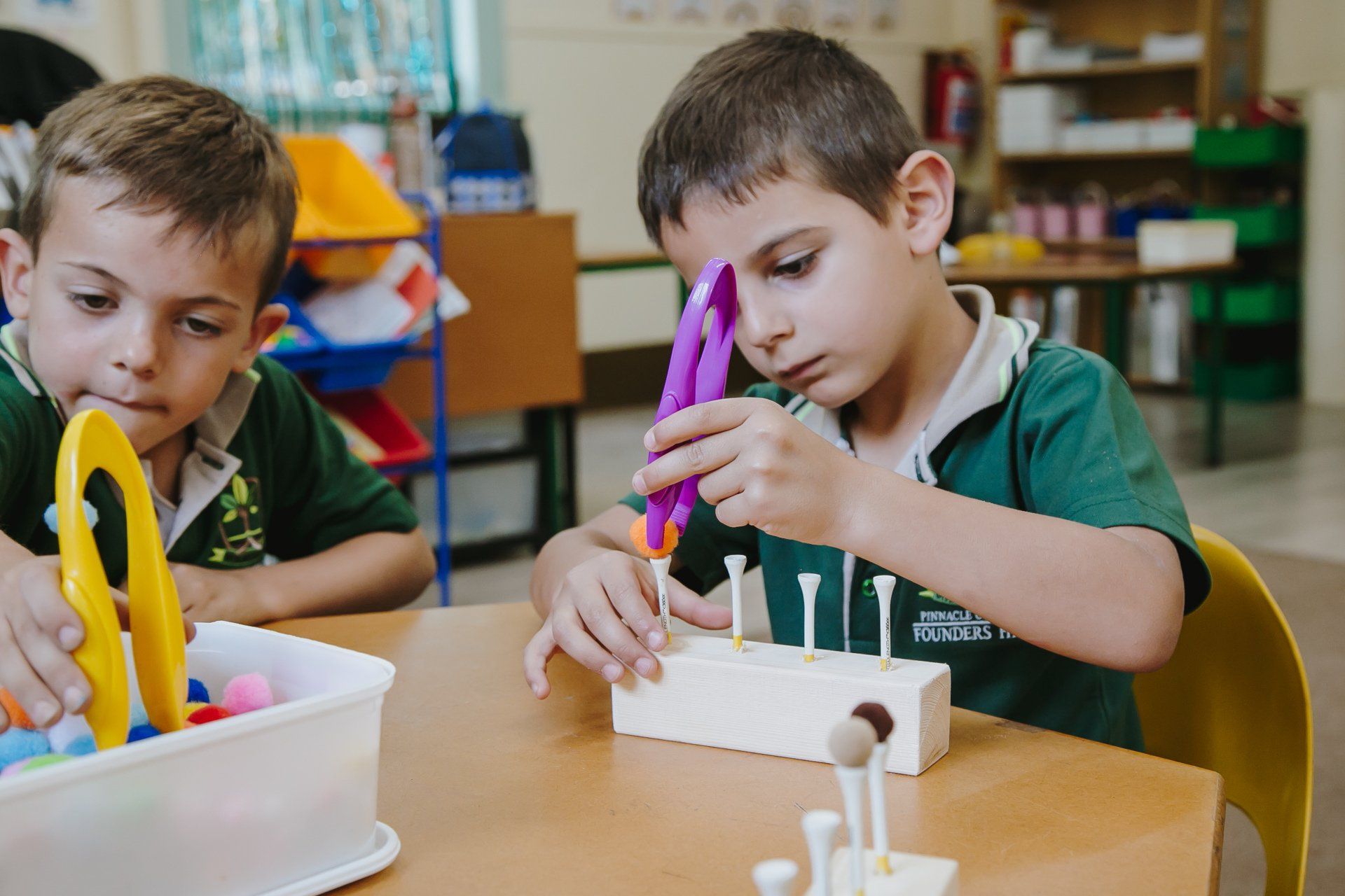 Two young boys are playing with toys at a table in a classroom.
