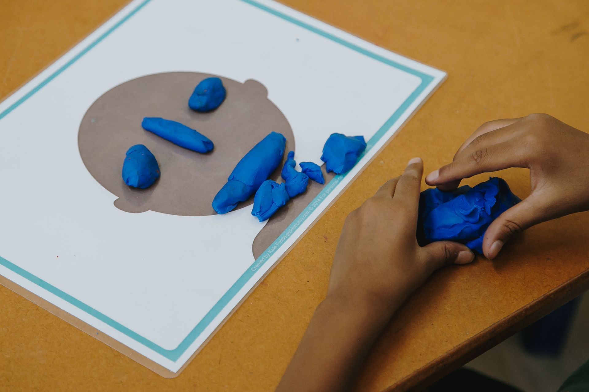 A child is playing with blue play dough on a table.