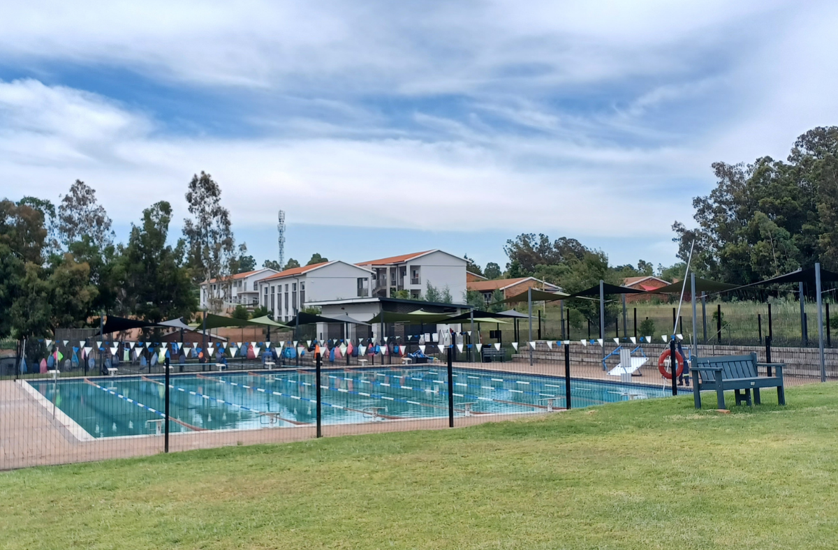 A large swimming pool is surrounded by a fence and a picnic table.