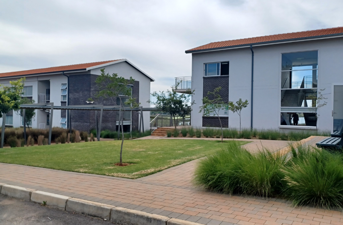 A white building with a red roof is next to a brick building with a lawn in front of it.