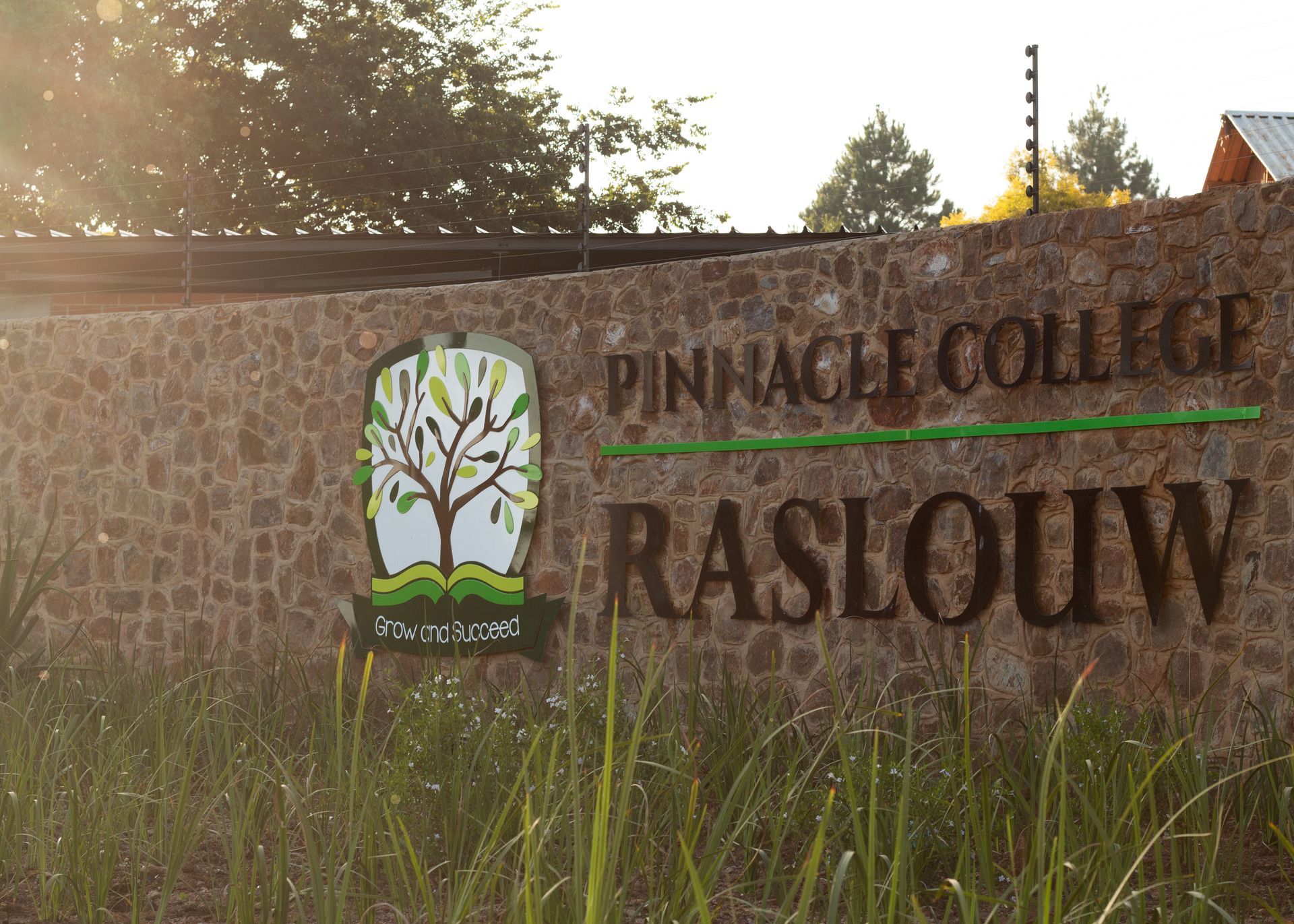 A sign for pinnacle college raslouw is on a stone wall