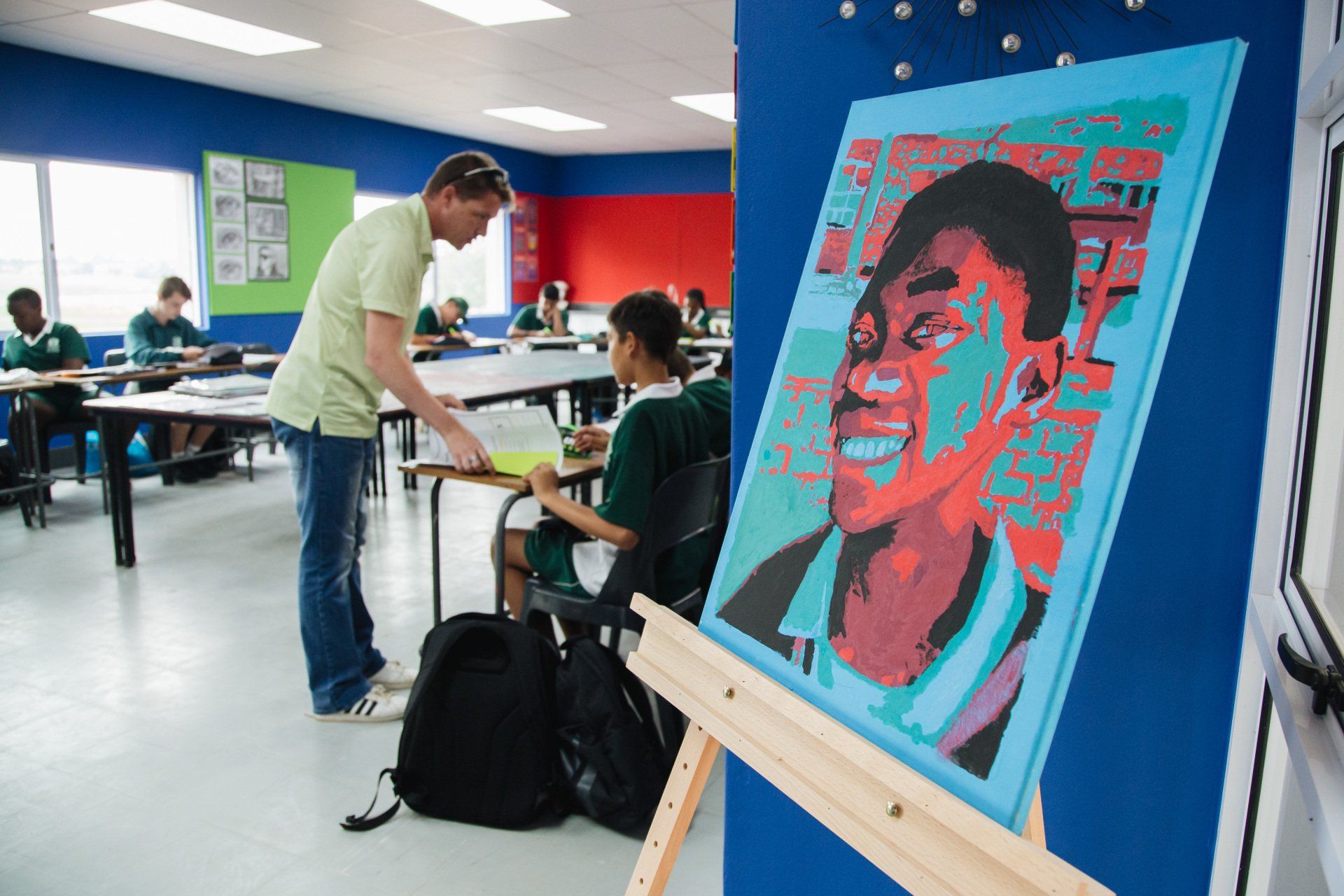 A man is standing next to a painting of a boy in a classroom.
