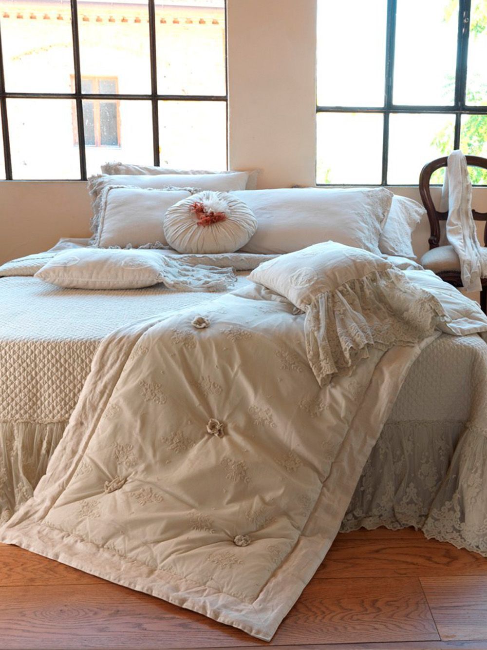 Letto con biancheria color crema, cuscini e trapunta inclusi, accanto a una finestra.