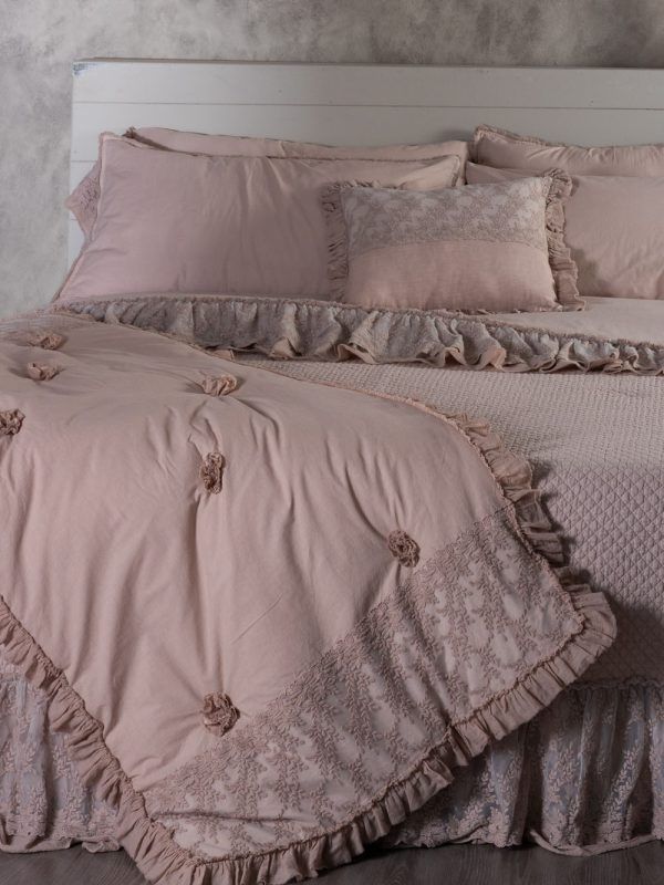 Letto con lenzuola rosa, bordi in pizzo, coperta arricciata e cuscini. Testiera bianca.