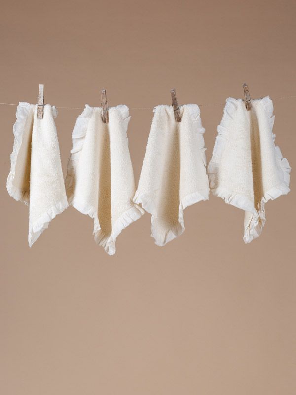 Quattro panni bianchi arricciati appesi a uno stendino, fermati con mollette di legno, sfondo beige.