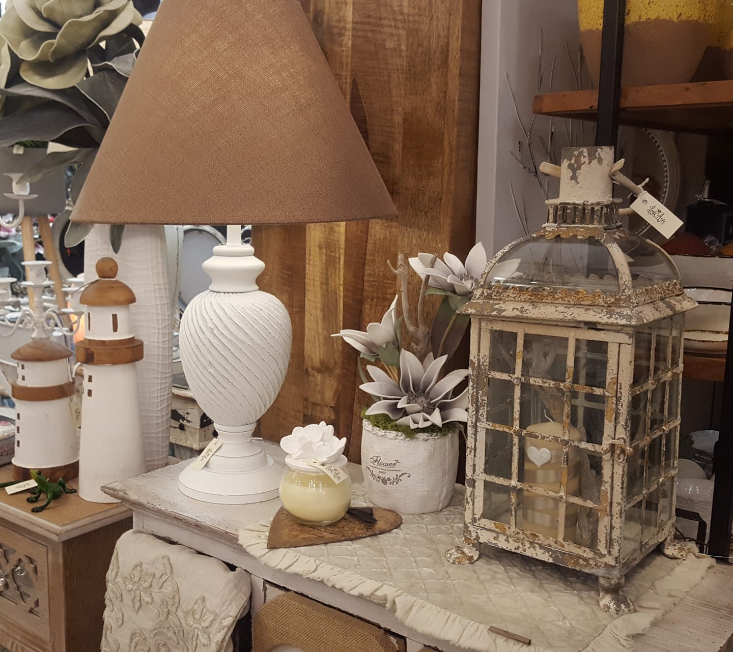 Lampada bianca, lanterna e decorazioni su un mobile anticato. Paralume beige, fiori finti e dettagli a forma di faro.