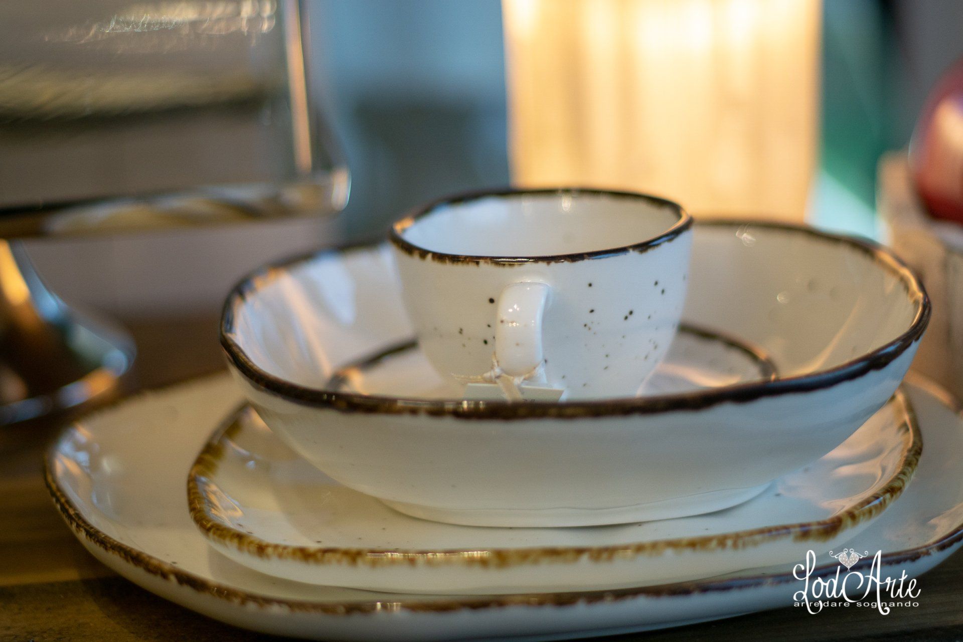 Set di stoviglie in ceramica bianca e marrone: tazza piccola, ciotola e piatto impilati su una superficie di legno.
