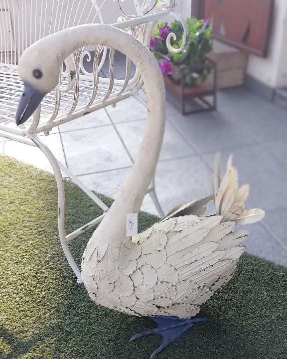 Scultura in metallo raffigurante un cigno bianco sporco, con becco e zampe blu, appoggiata su erba artificiale.