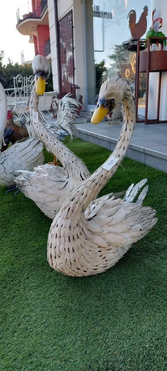 Due statue di cigni realizzate in materiale intrecciato su un manto erboso verde. Becchi gialli e colli lunghi.