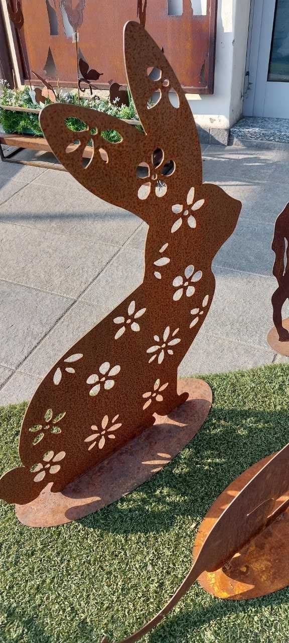 Scultura di un coniglietto in metallo arrugginito con ritagli di fiori, in piedi sull'erba.