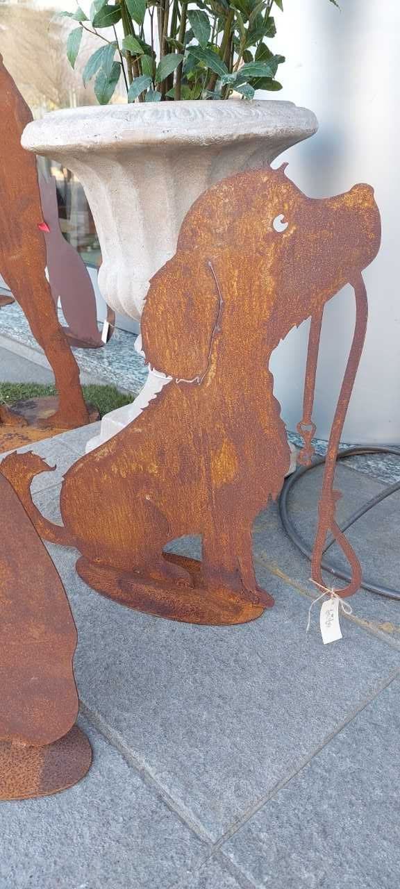 Scultura in metallo color ruggine raffigurante un cane che tiene un guinzaglio, seduto su una superficie di pietra grigia.