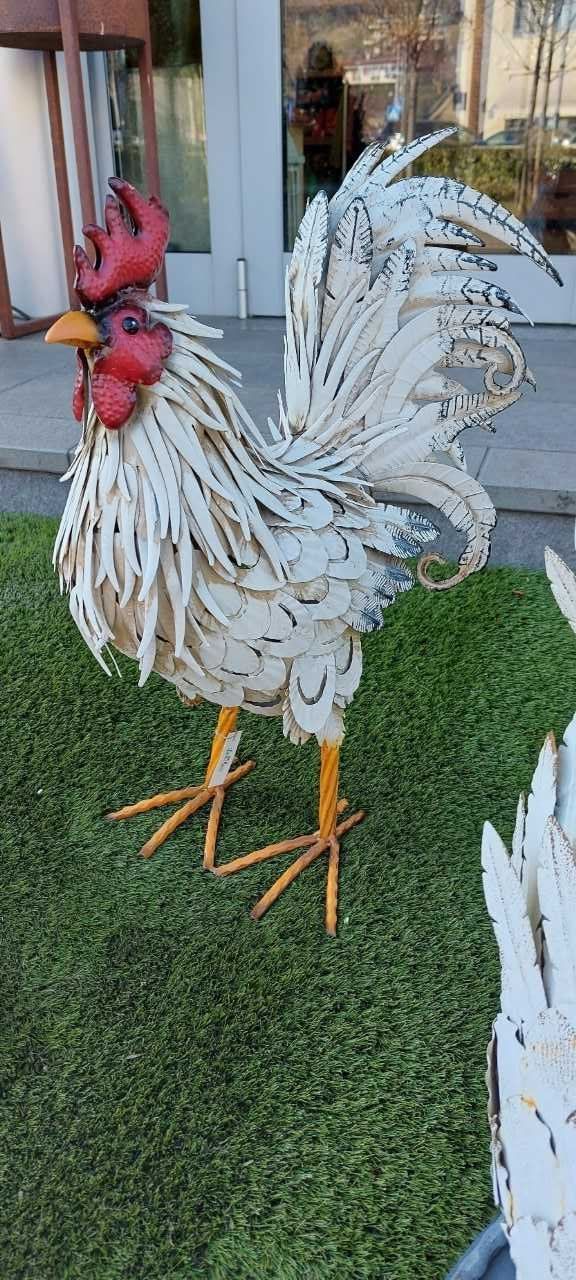 Scultura in metallo di un gallo con cresta rossa, becco e zampe gialle, su erba verde.