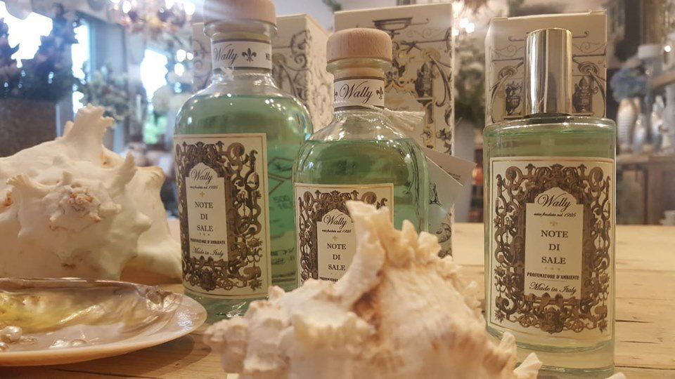 Flaconi di profumo verde chiaro con etichette decorate, esposti insieme a conchiglie su un tavolo di legno.