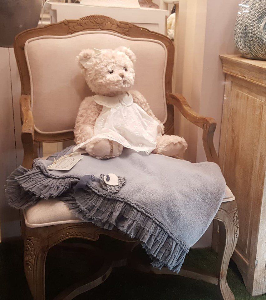Un orsacchiotto vestito di bianco è seduto su una sedia, avvolto in una coperta blu.