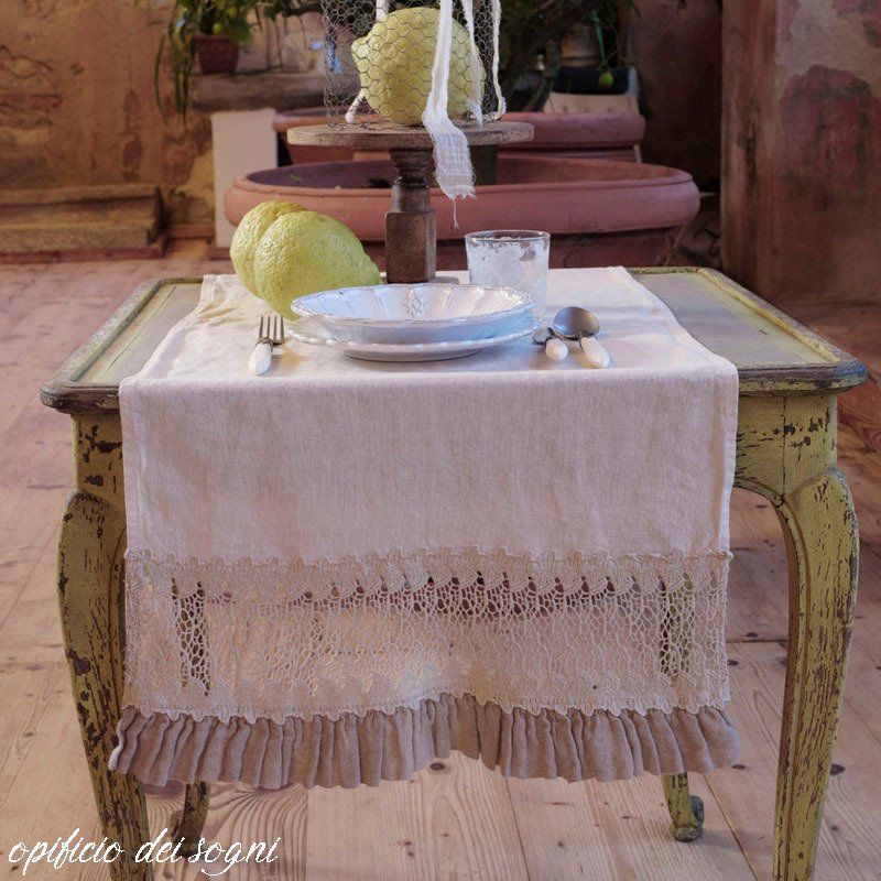 Apparecchiatura da tavola con runner di lino, bordi in pizzo e volant, decorata con limoni e stoviglie.