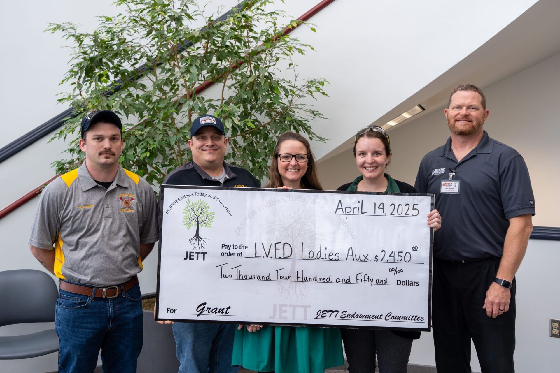 Five people holding a large check in an office lobby; check reads
