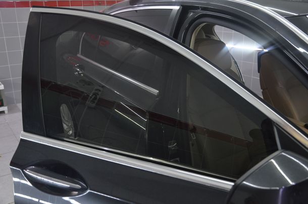 Dark gray car side window and door in a showroom or garage.