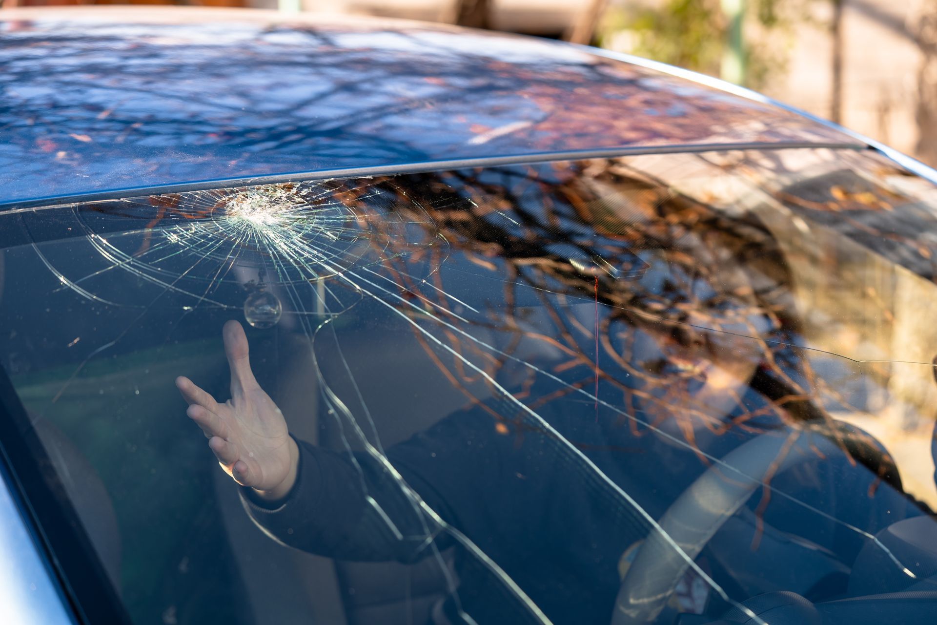 Cracked car windshield with a person inside raising a finger
