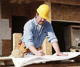 Construction worker wearing a yellow hard hat, reviewing blueprints at a construction site.