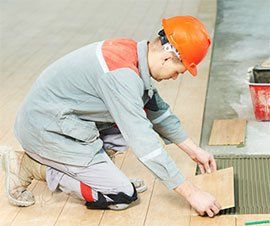 Construction worker in orange hard hat installing floor tiles.
