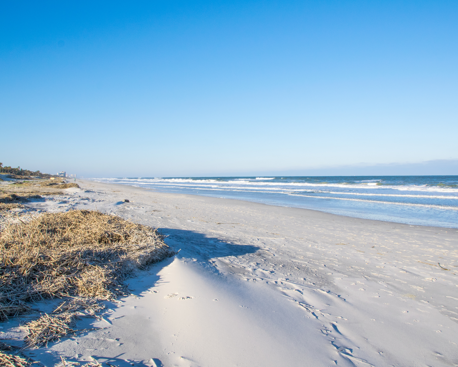 Sandy beach under a clear blue sky, with waves crashing in the distance.