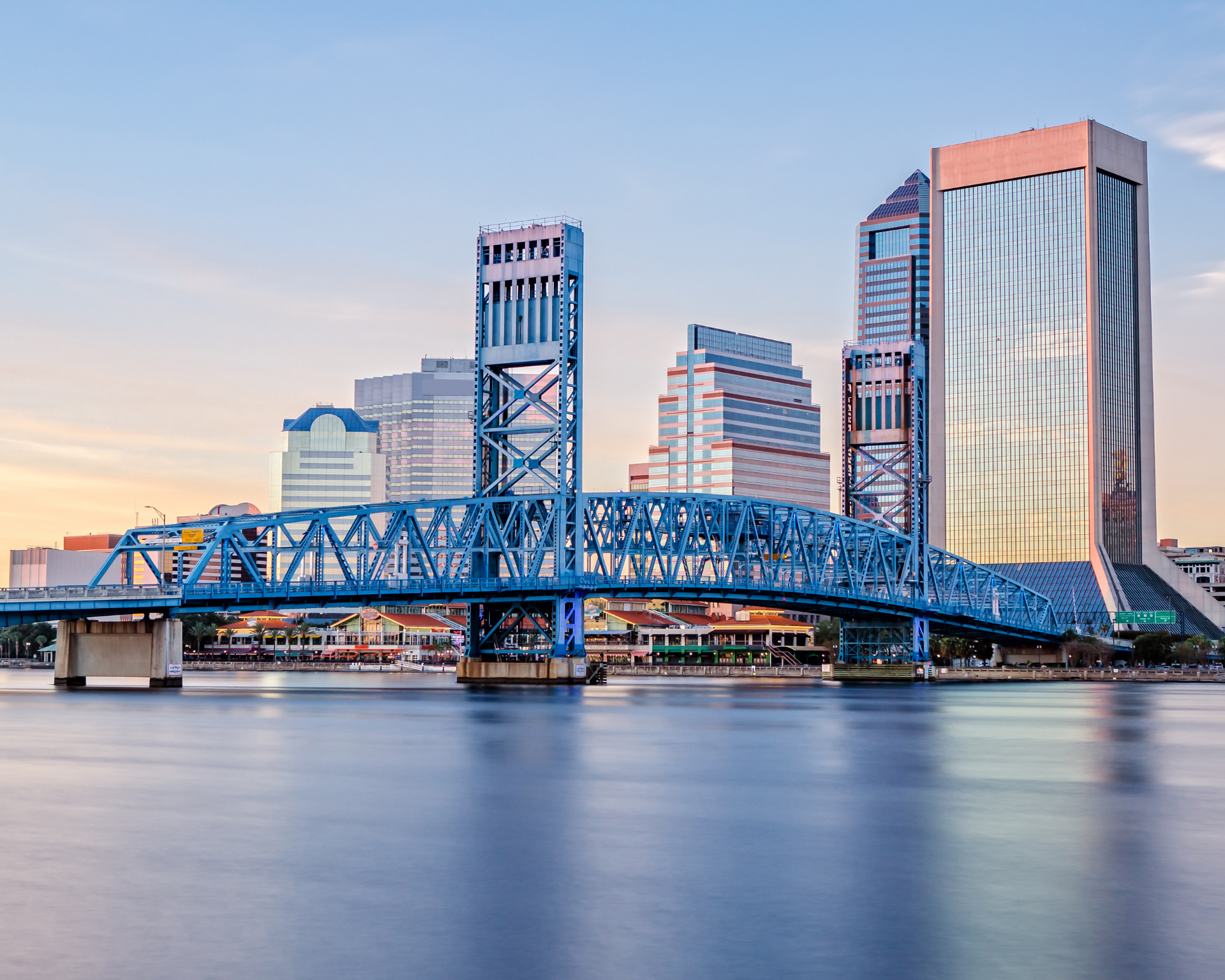 Blue bridge over water with Jacksonville, Florida skyline in background.