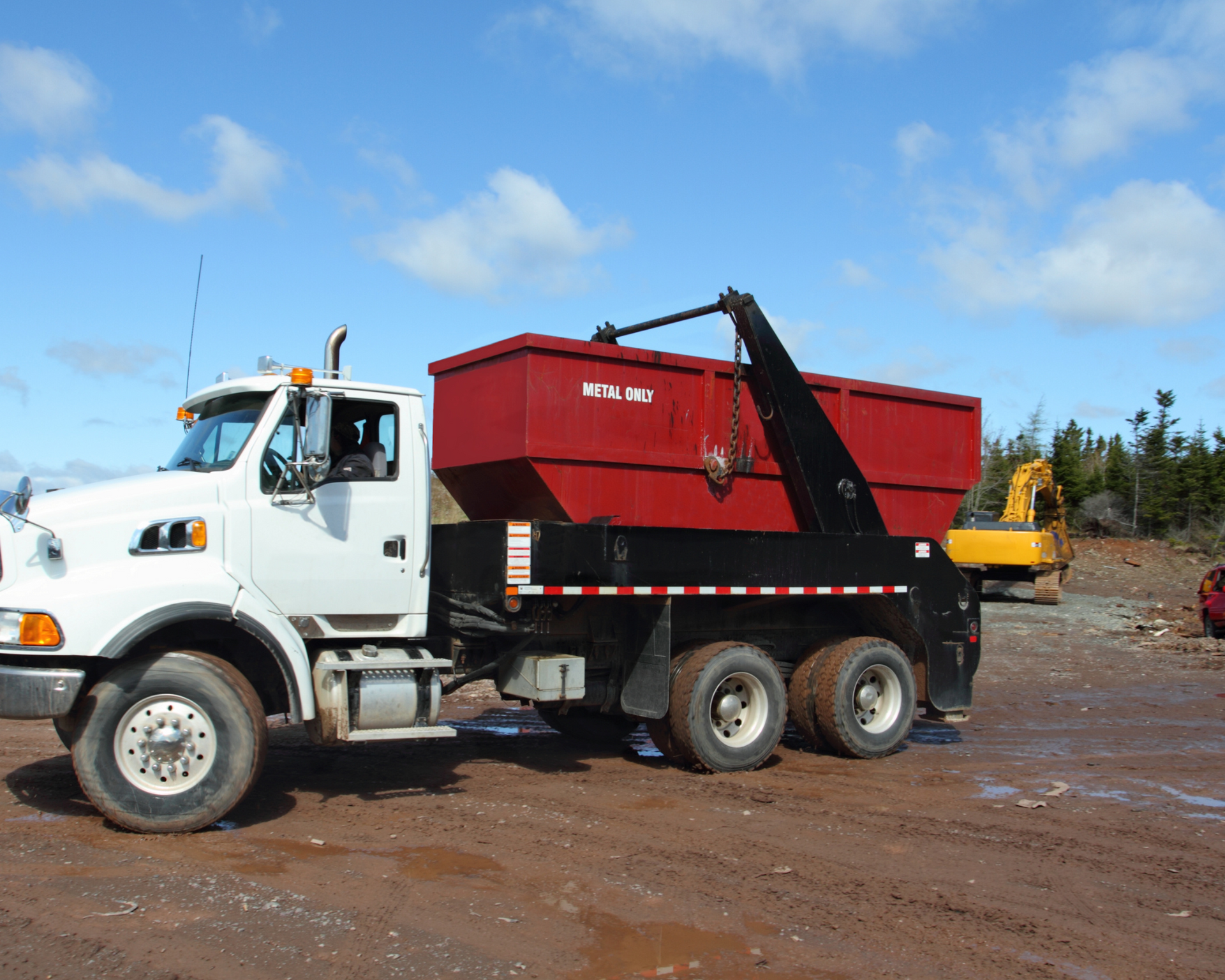 White dump truck with a red container in a dirt lot under a blue sky.