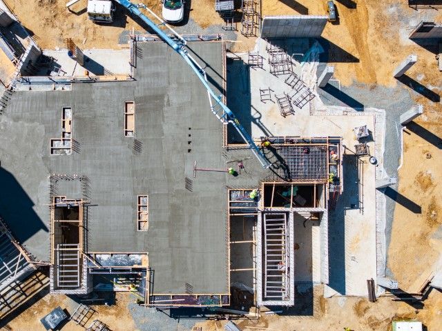 Aerial view of a building under construction with a gray roof, scaffolding, and workers.
