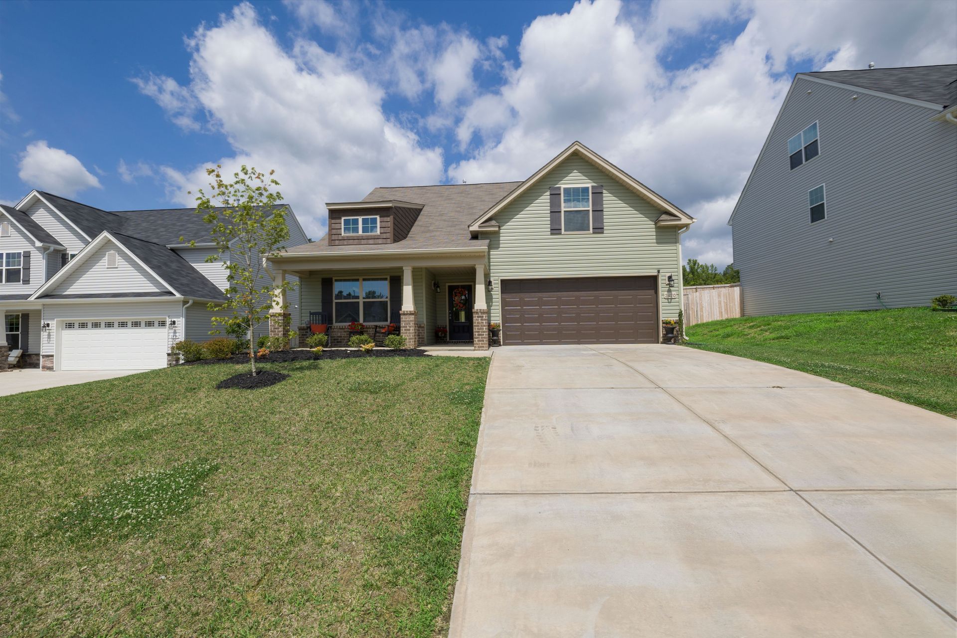 Suburban house with brown garage door, front porch, and sloped driveway under a partly cloudy sky