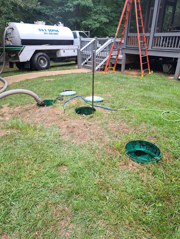White utility truck by a grassy yard with open manholes and a metal platform in the background