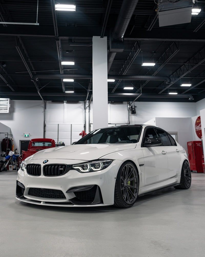 White BMW sedan in a workshop, lowered with black rims and a front lip