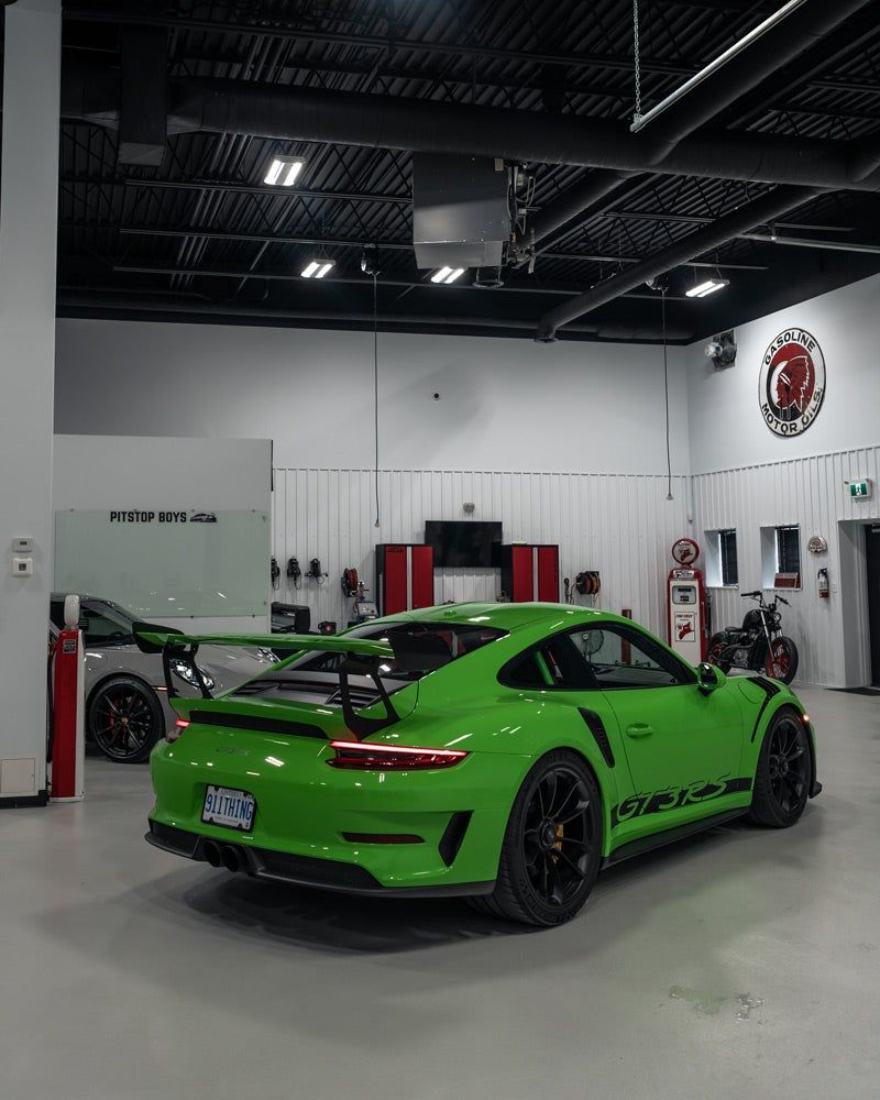 Bright green sports car in a garage, viewed from the rear with a large black spoiler.