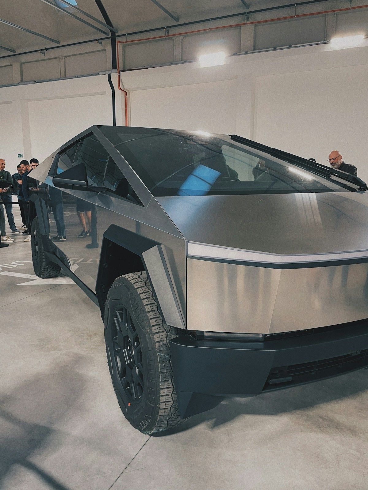 Tesla Cybertruck on display in a warehouse, showing its angular silver body and black wheels.