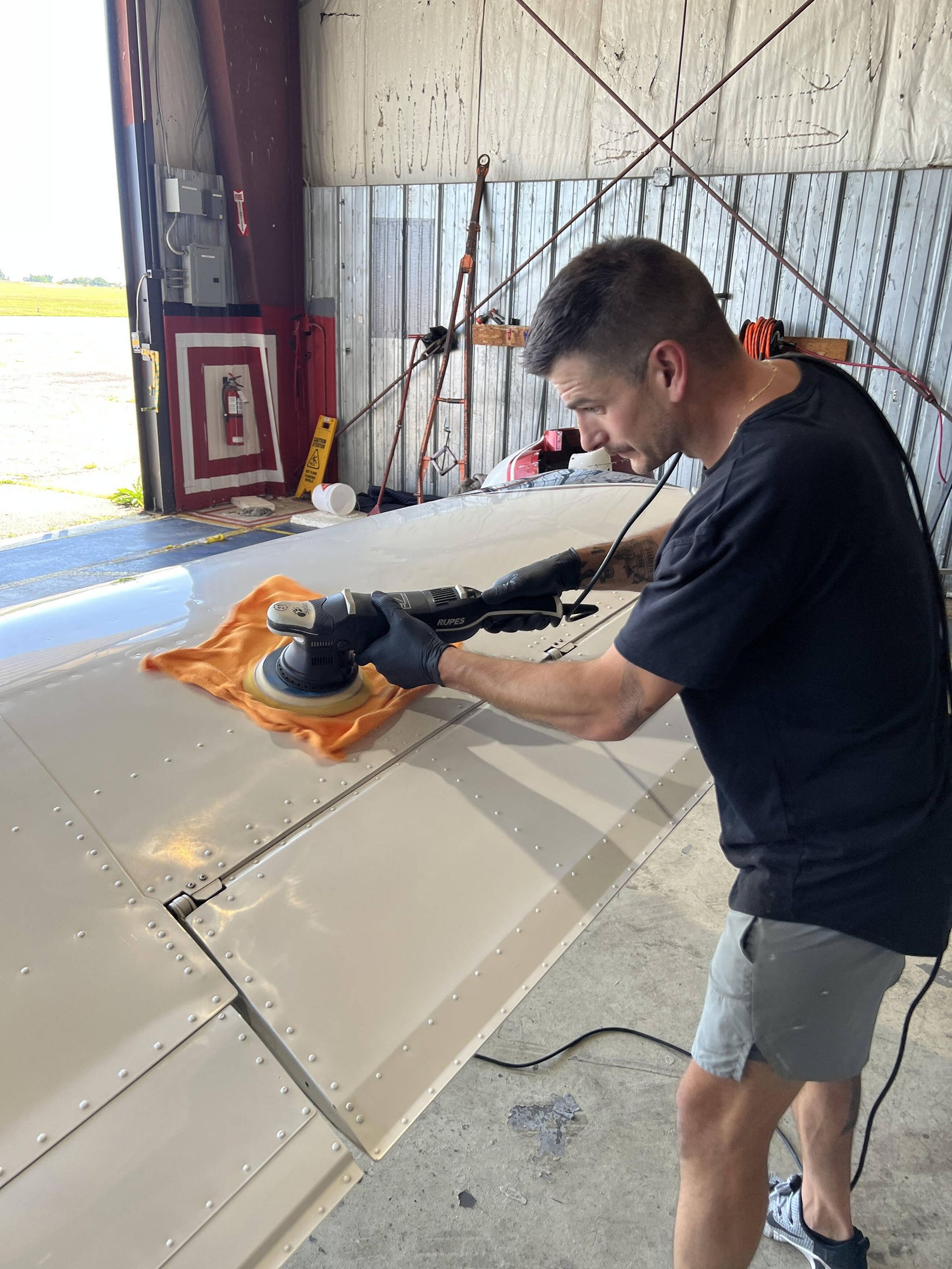 Person using a tool to cut or trim a sheet of orange insulation foam inside a large workshop