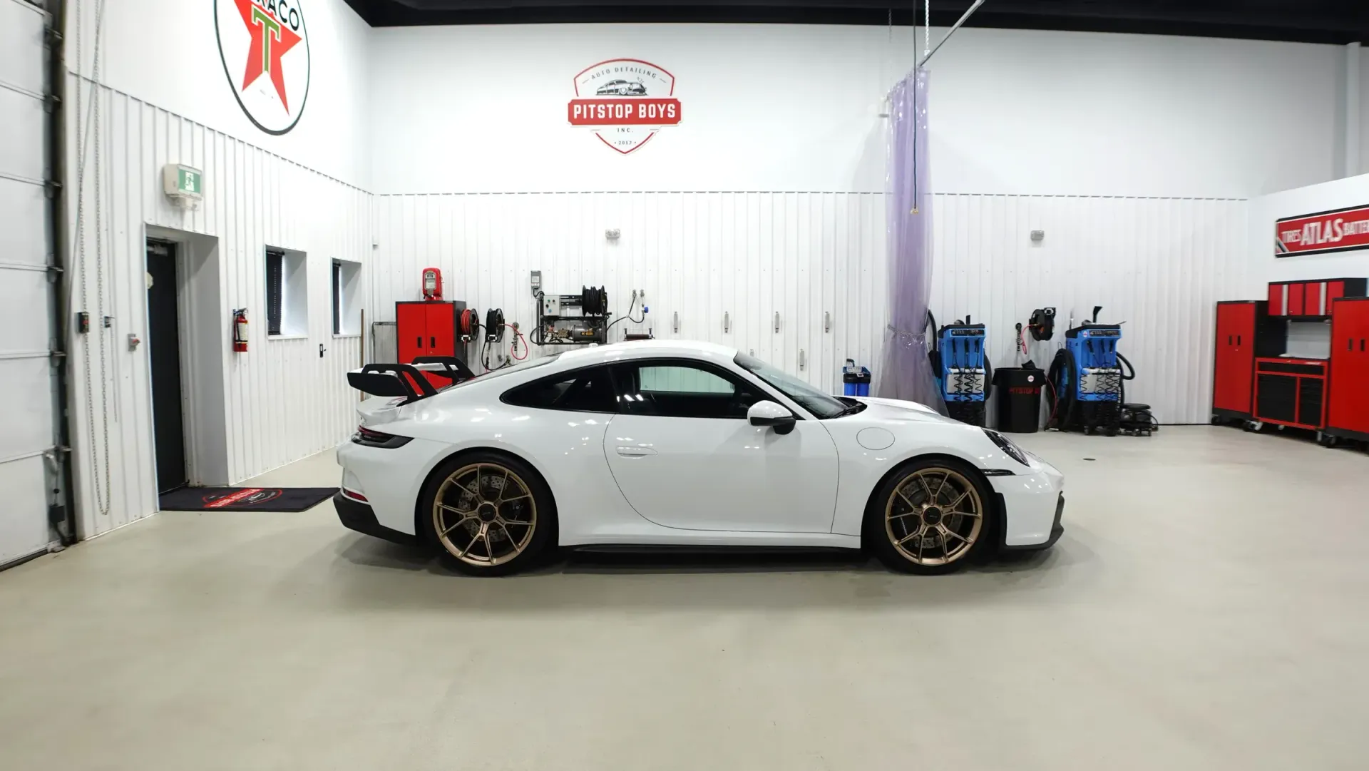 White sports car in a bright auto shop, shown in side profile with red and black accents.