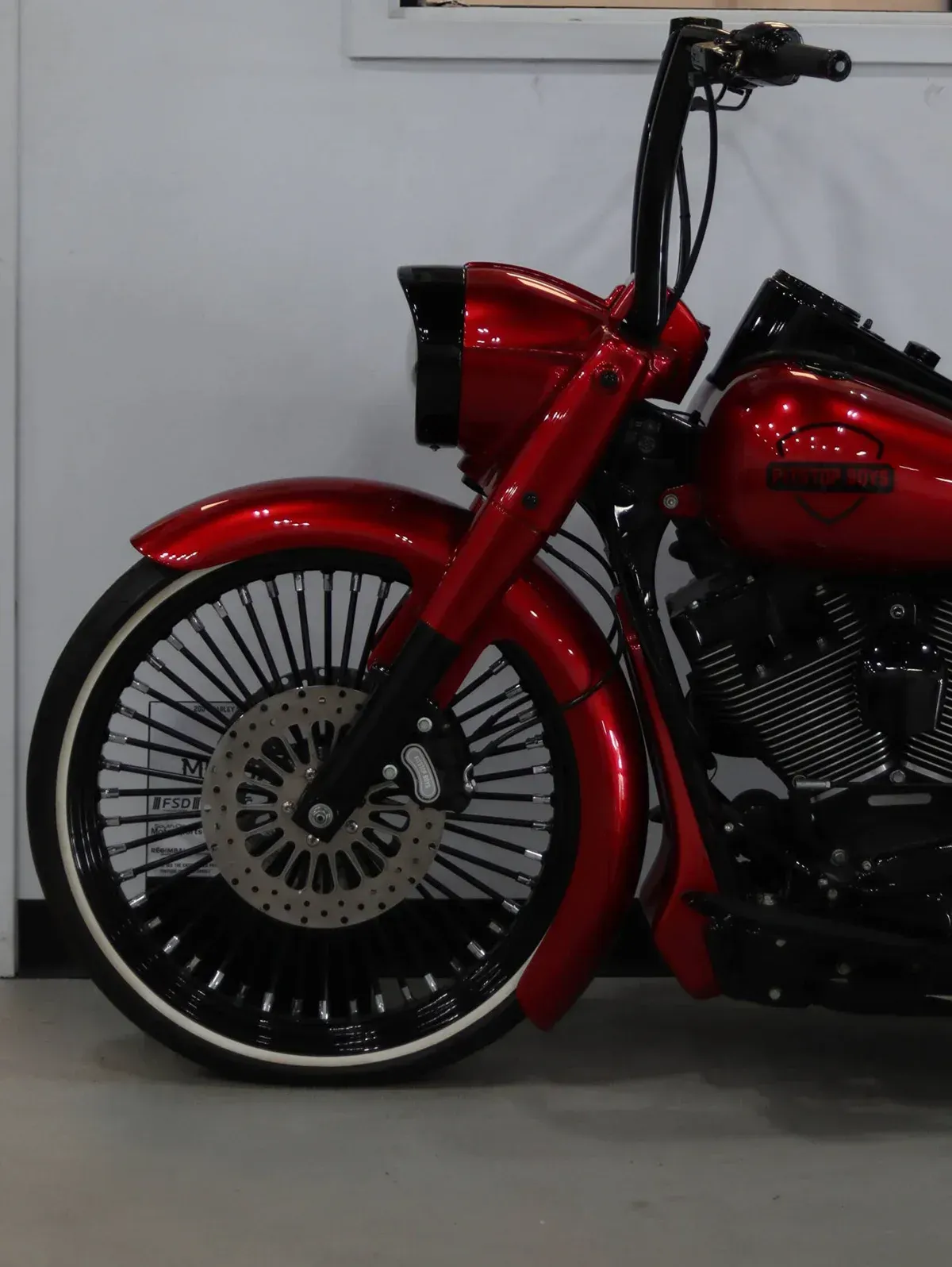 Red custom motorcycle with glossy red body and spoked front wheel, parked indoors against a gray wall
