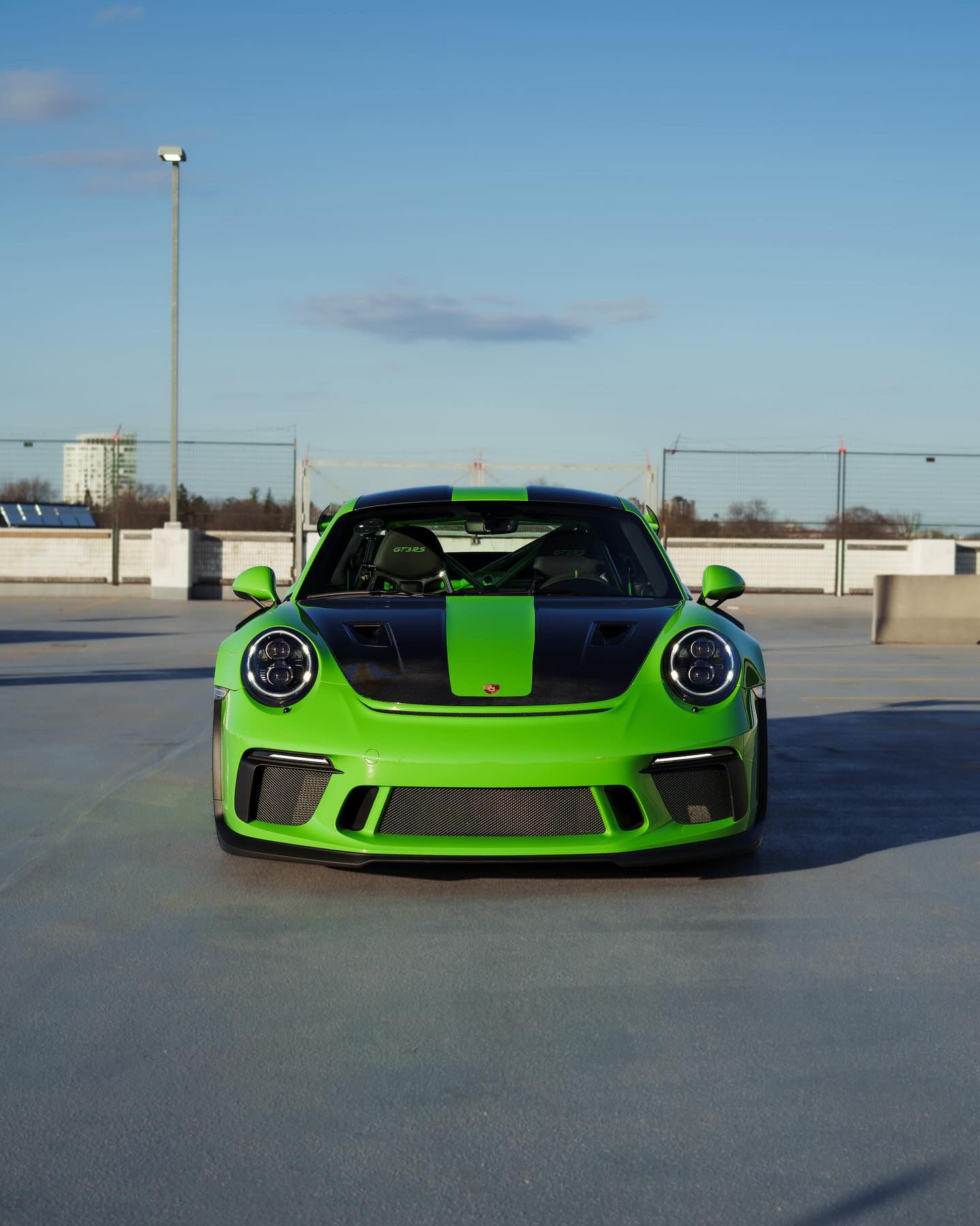 Bright green sports car parked on an open lot, front view with black racing stripe.